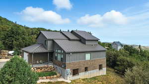 Rear view of property featuring brick siding, a metal roof, driveway, and an attached garage