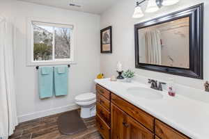 Bathroom featuring visible vents, baseboards, toilet, wood finish floors, and vanity