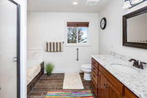 Bathroom with toilet, vanity, a garden tub, a shower stall, and baseboards
