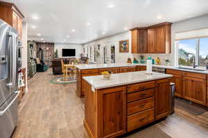 Kitchen featuring wood finished floors, a sink, stainless steel refrigerator with ice dispenser, open floor plan, and a wood stove