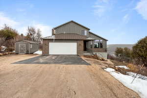 View of front of house with a standing seam roof, an attached garage, metal roof, driveway, and brick siding