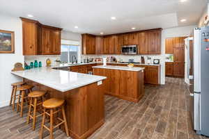 Kitchen featuring a sink, a peninsula, appliances with stainless steel finishes, brown cabinetry, and wood tiled floor