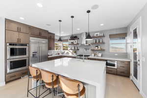 Kitchen with wall chimney exhaust hood, light wood-style flooring, open shelves, appliances with stainless steel finishes, and backsplash