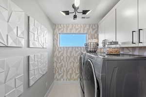 Laundry room featuring separate washer and dryer, visible vents, wallpapered walls, baseboards, and cabinet space