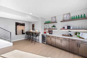 Bar featuring baseboards, a bar, wine cooler, recessed lighting, and light wood-style flooring