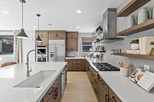 Kitchen featuring open shelves, wall chimney exhaust hood, decorative backsplash, stainless steel appliances, and a sink