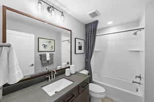 Full bathroom featuring a textured ceiling, shower / bathtub combination with curtain, vanity, visible vents, and toilet