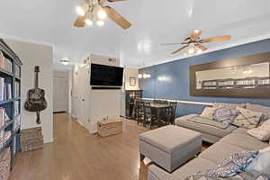 Living area featuring visible vents, ceiling fan with notable chandelier, crown molding, and wood finished floors