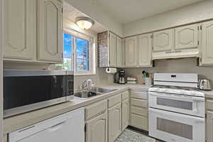 Kitchen featuring a sink, light countertops, white appliances, and under cabinet range hood