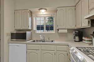 Kitchen featuring a sink, light countertops, white appliances, and under cabinet range hood