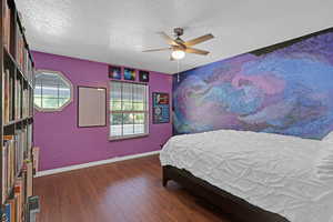 Bedroom with baseboards, multiple windows, wood finished floors, and a textured ceiling