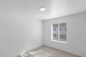 Spare room featuring visible vents, light carpet, and baseboards