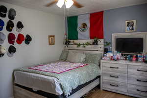 Bedroom with a textured ceiling, wood finished floors, and a ceiling fan