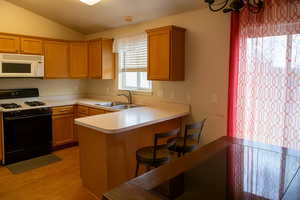 Kitchen with white microwave, vaulted ceiling, gas stove, a sink, and light wood finished floors