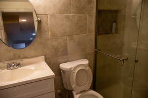 Full bath featuring toilet, a stall shower, vanity, and tile walls
