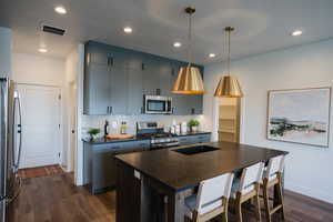 Kitchen with dark wood-style floors, visible vents, dark countertops, stainless steel appliances, and backsplash