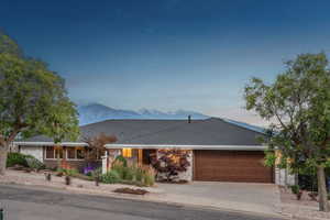 Ranch-style house featuring an attached garage, driveway, stone siding, and roof with shingles