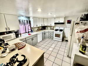Kitchen featuring under cabinet range hood, light countertops, a sink, light tile patterned floors, and white appliances