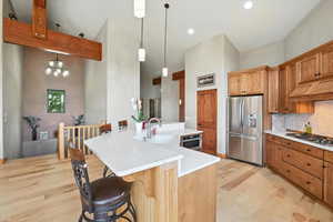 Kitchen featuring stainless steel appliances, light wood finished floors, custom exhaust hood, light countertops, and a breakfast bar