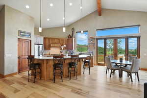 Kitchen with high vaulted ceiling, stainless steel refrigerator with ice dispenser, light wood finished floors, beam ceiling, and light countertops