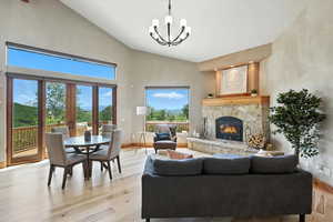 Living room with high vaulted ceiling, a chandelier, light wood-style floors, and a stone fireplace