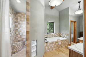 Full bath featuring a bath, wood finished floors, vanity, tiled shower, and high vaulted ceiling