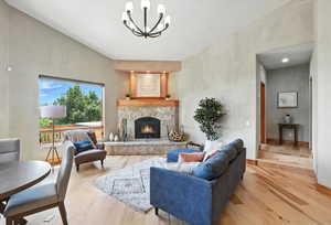 Living room featuring light wood finished floors, a chandelier, and a stone fireplace