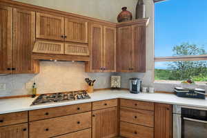Kitchen with stainless steel appliances, brown cabinetry, backsplash, and light countertops