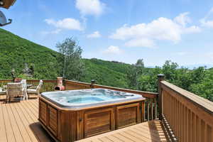 Deck with a hot tub, outdoor dining space, and a wooded view