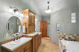 Bathroom with a tub to relax in, vanity, wood finished floors, and lofted ceiling