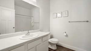 Bathroom featuring vanity, toilet, a shower, wood finished floors, and baseboards