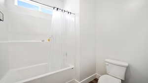 Full bath featuring toilet, shower / tub combo with curtain, wood finished floors, and baseboards