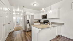 Kitchen with baseboards, a sink, a peninsula, dark wood finished floors, and stainless steel appliances