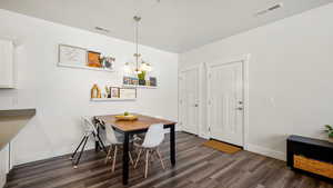 Dining space with a notable chandelier, baseboards, visible vents, and dark wood finished floors