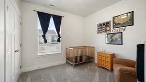 Carpeted bedroom featuring baseboards, visible vents, and a crib