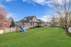 Rear view of property with a trampoline, a fenced backyard, a playground, and a lawn
