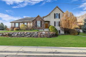 View of front of house featuring a front lawn, stone siding, and stucco siding