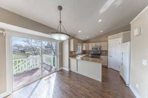 Kitchen with tasteful backsplash, dark wood-style flooring, a peninsula, lofted ceiling, and appliances with stainless steel finishes, granit counter tops