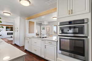 Kitchen with light countertops, white cabinetry, black electric cooktop, built in microwave and oven