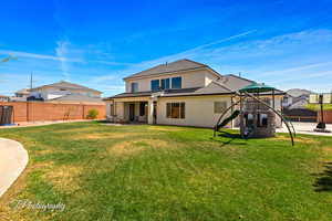 Rear view of house featuring stucco siding, a lawn, a patio, fence, and a playground
