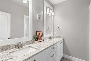 Full bath featuring wood finished floors, double vanity, a sink, and baseboards