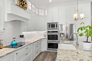 Kitchen with dark wood-style floors, white cabinets, appliances with stainless steel finishes, a sink, and hanging light fixtures