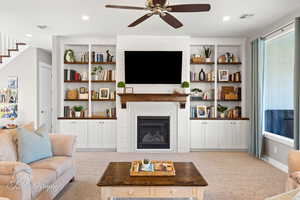 Carpeted living area featuring visible vents, ceiling fan, a brick fireplace, and stairs
