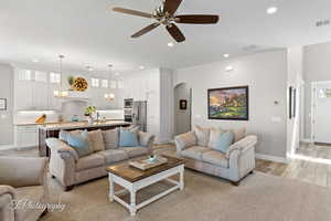 Living room with light wood-style floors, arched walkways, a ceiling fan, visible vents, and recessed lighting