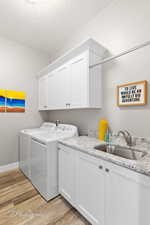 Clothes washing area with light wood-style flooring, washing machine and dryer, a sink, baseboards, and cabinet space