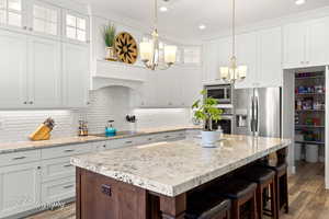 Kitchen featuring dark wood-style flooring, a chandelier, glass insert cabinets, white cabinetry, and appliances with stainless steel finishes
