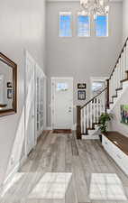 Entrance foyer with stairs, a notable chandelier, a towering ceiling, and light wood-type flooring
