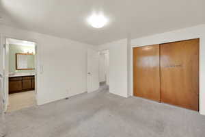 Unfurnished bedroom with ensuite bath, a closet, baseboards, and light colored carpet