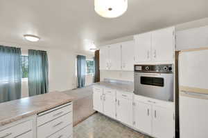 Kitchen with oven, light countertops, white cabinetry, and freestanding refrigerator