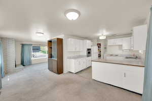 Kitchen featuring white cabinets, oven, a sink, a peninsula, and light carpet